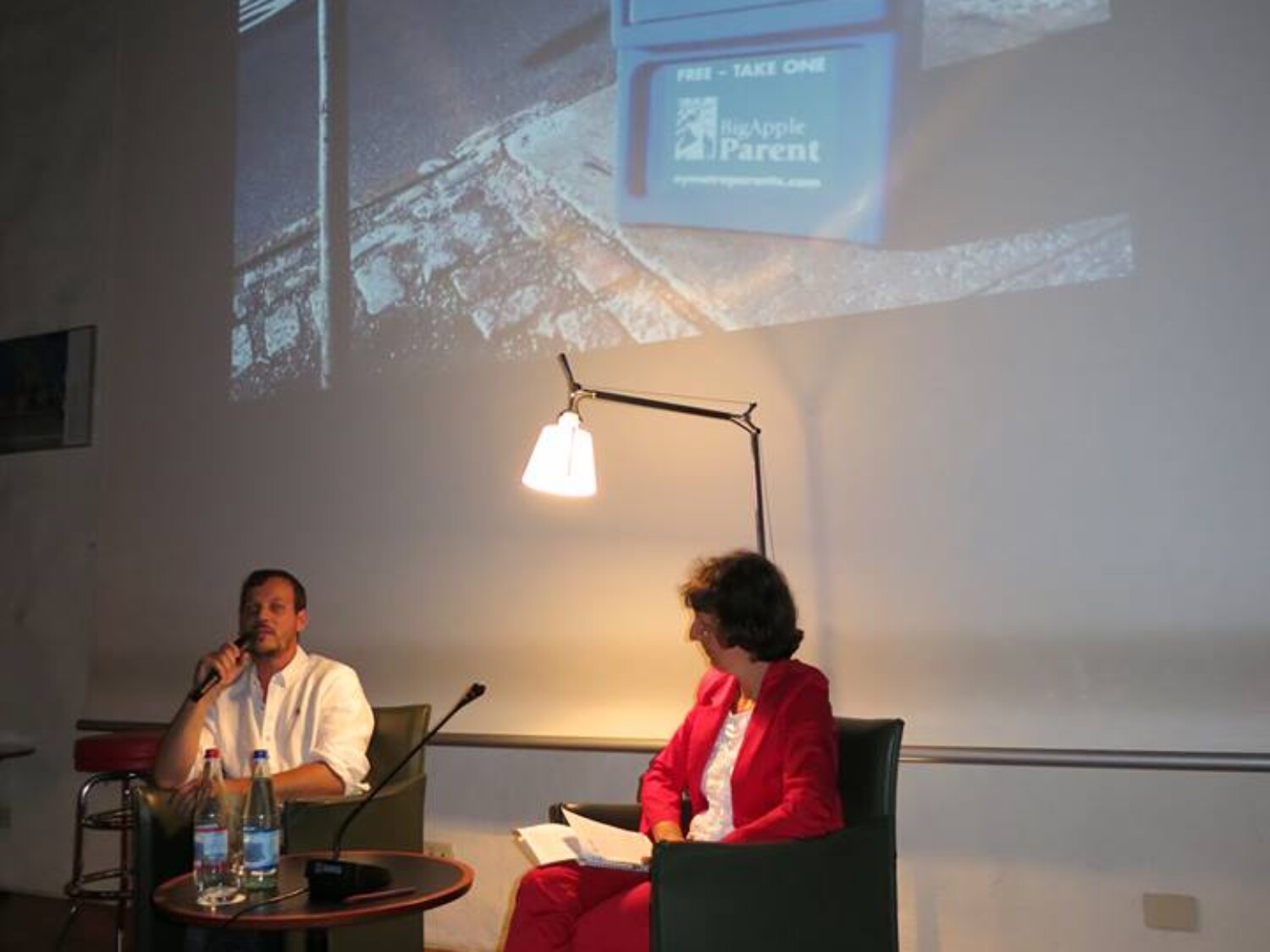 a man and woman sitting in chairs and talking on a projector screen. Carlo Sampietro