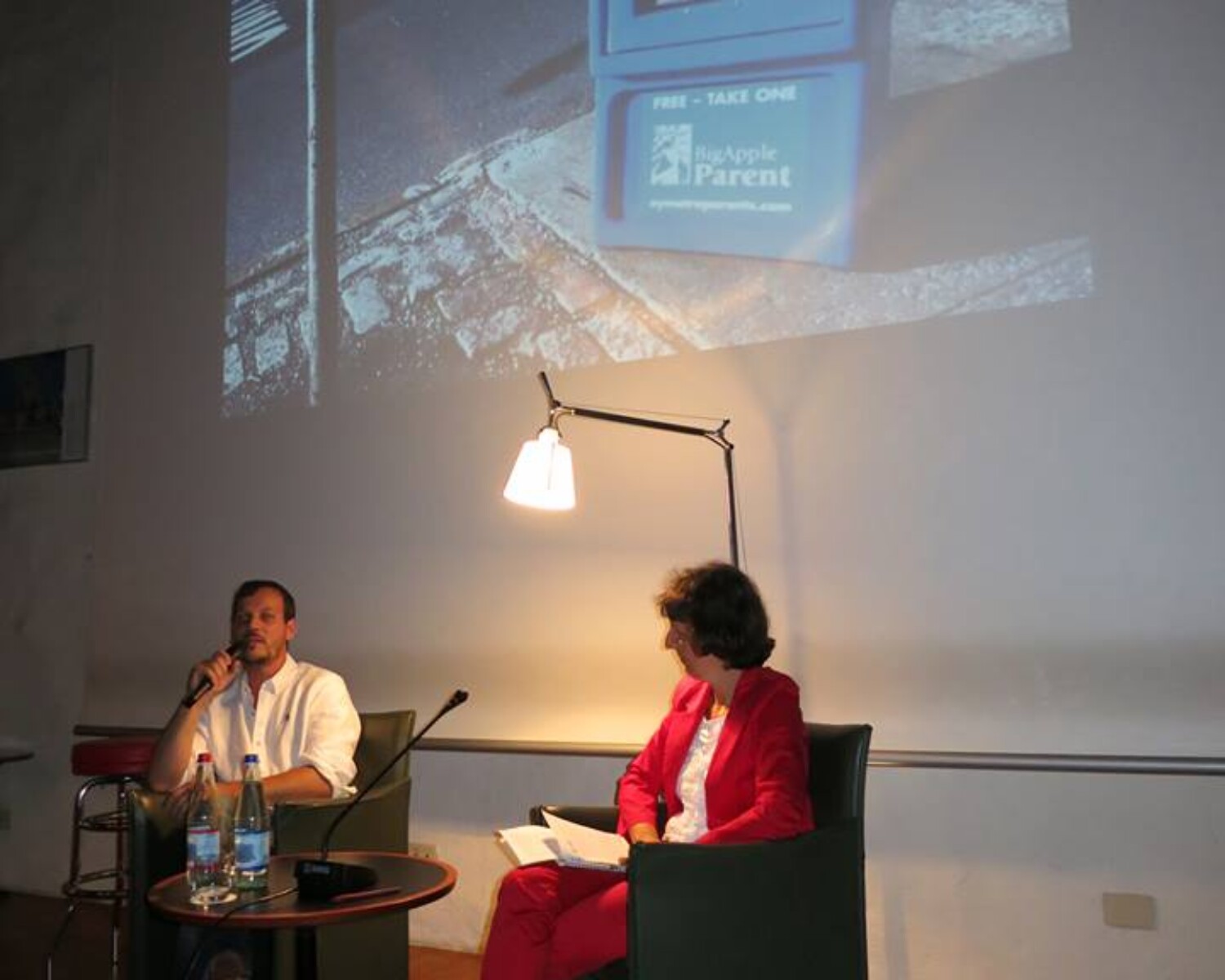 a man and woman sitting in chairs and talking on a projector screen. Carlo Sampietro